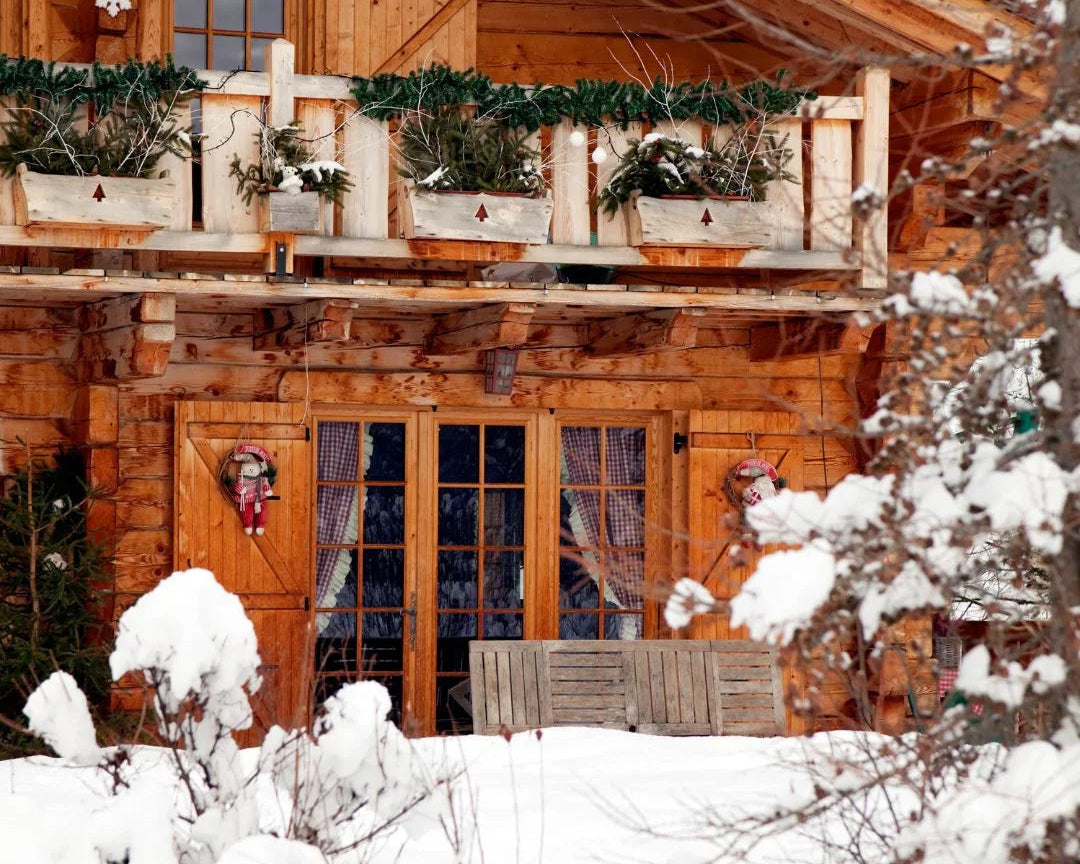 Chalet en bois enneigé avec balcon décoré de sapins et rueurs de Noël hivernale