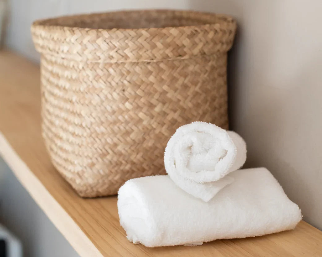 Panier en osier tressé et serviettes blanches pliées sur étagère en bois clair