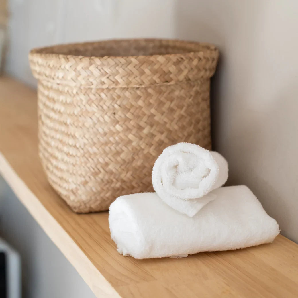 Serviettes blanches en coton doux pour hôtel, rangées sur étagère en bois avec panier tressé