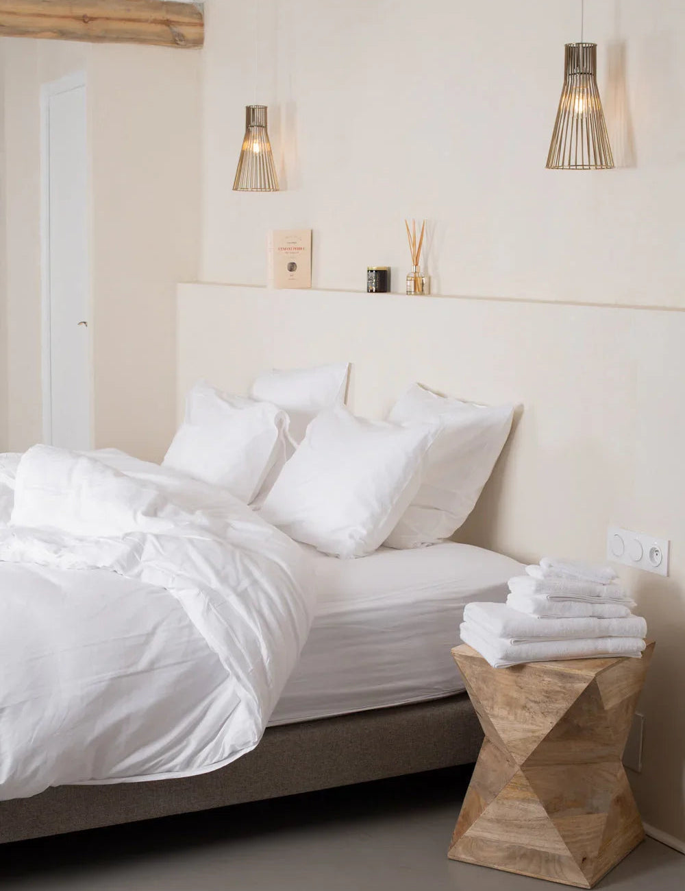 Chambre minimaliste avec lit blanc, coussins moelleux, table en bois sculpté et suspension lumineuse