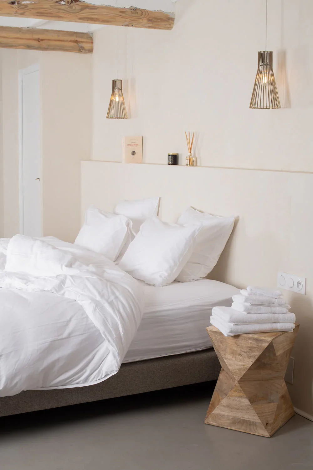 Chambre minimaliste avec lit blanc, coussins moelleux, table en bois sculpté et suspension lumineuse