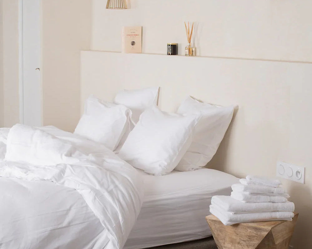 Chambre minimaliste avec lit blanc, coussins moelleux, table en bois sculpté et suspension lumineuse