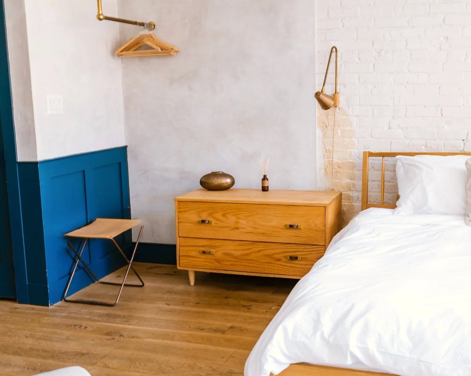 Chambre moderne avec lit en bois clair, couverture blanche, commode et mur blanc avec peinture bleue