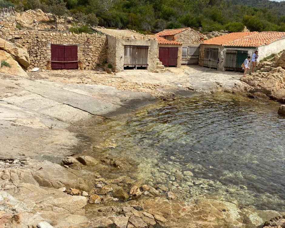 Cabanes en pierre au bord d'une eau claire avec rochers et deux personnes sur une côte rocheuse