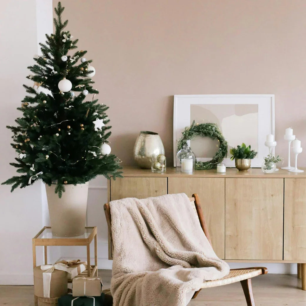 Salon décoré minimaliste avec sapin de Noël blanc et doré, fauteuil avec plaid beige