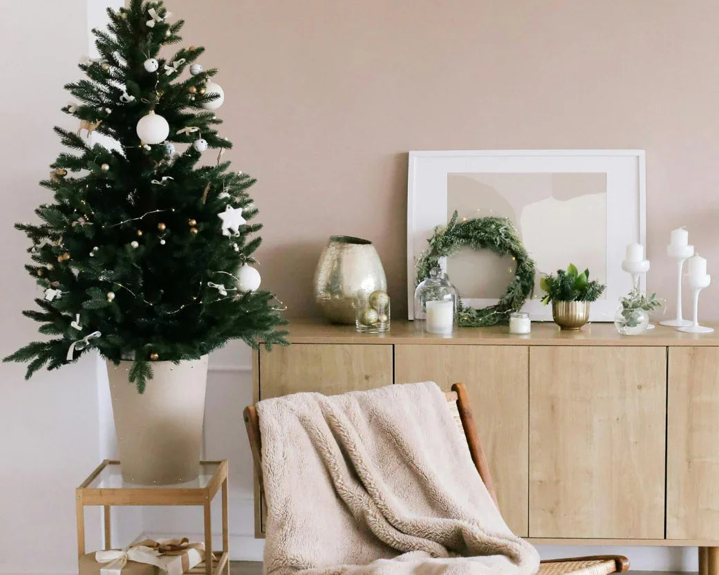 Salon décoré minimaliste avec sapin de Noël blanc et doré, fauteuil avec plaid beige