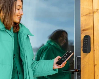 Femme utilisant smartphone pour déverrouiller porte en bois avec système numérique, idéal pour hôtels et maisons d'hôtes