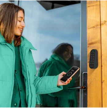 Femme utilisant smartphone pour déverrouiller porte en bois avec système numérique, idéal pour hôtels et maisons d'hôtes