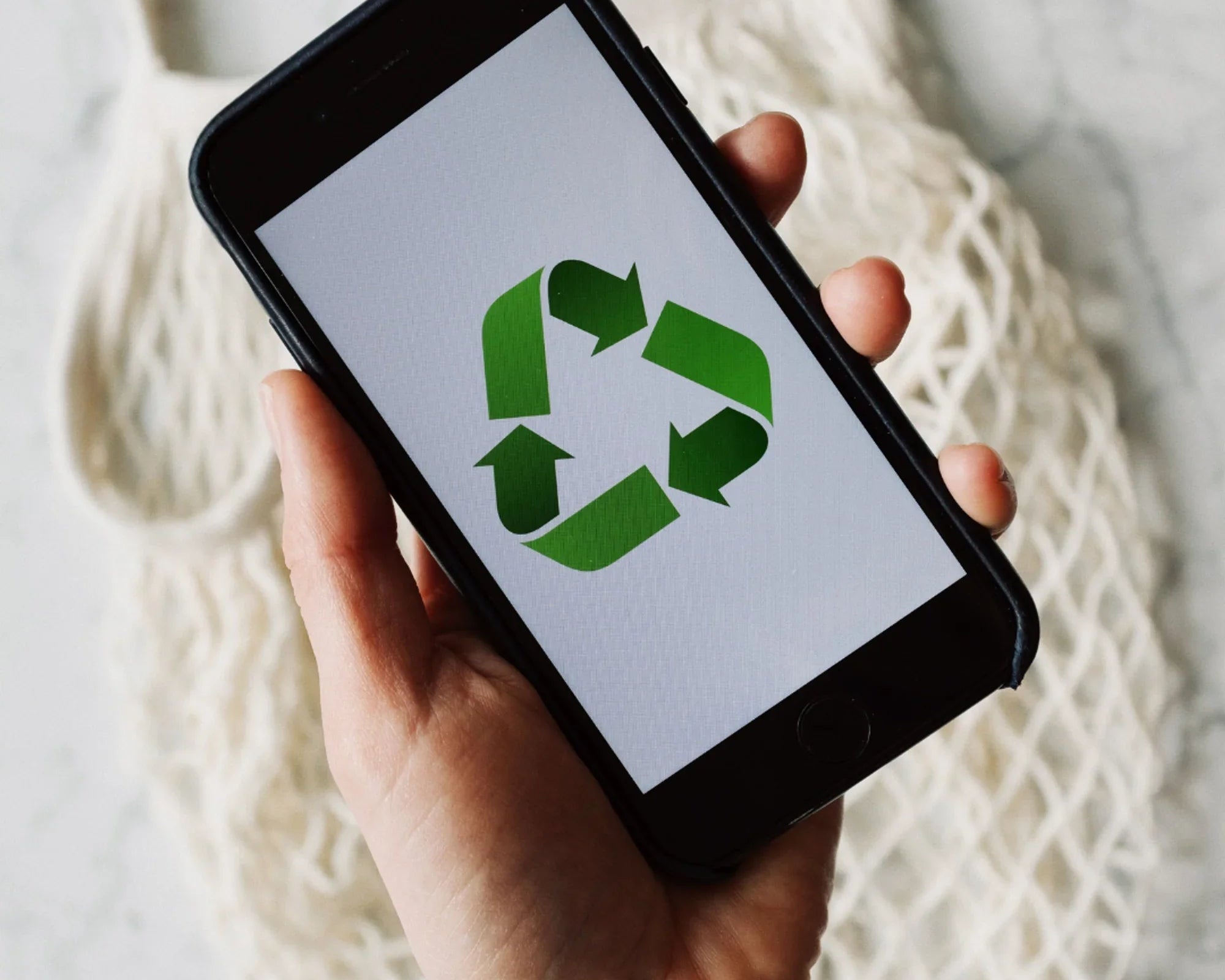 Main d'une personne tenant un smartphone affichant le symbole de recyclage vert sur fond blanc