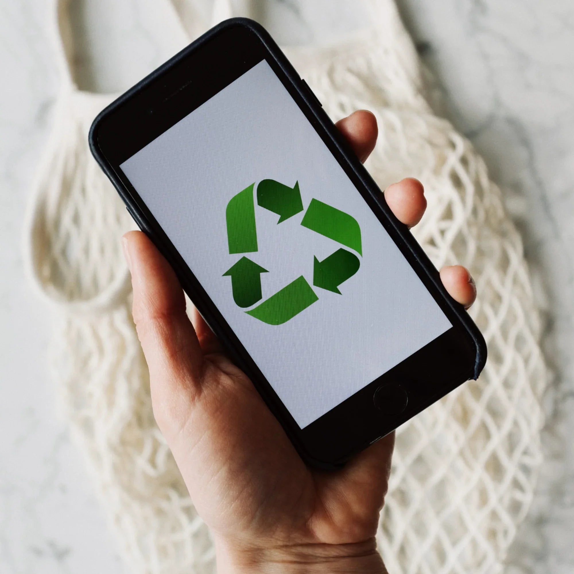 Main d'une personne tenant un smartphone affichant le symbole de recyclage vert sur fond blanc