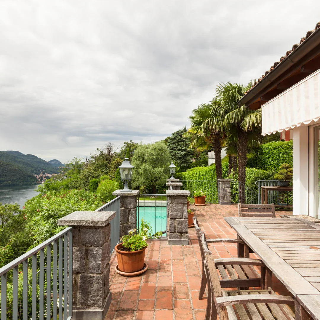Terrasse en pierre avec table en bois, plantes en pots, palmiers et vue sur lac et montagne