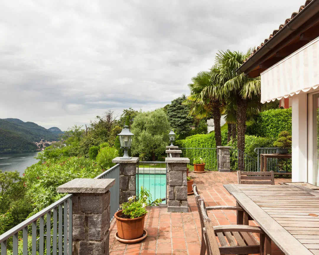 Terrasse en pierre avec table en bois, plantes en pots, palmiers et vue sur lac et montagne