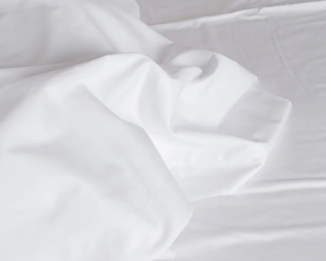 Draps en satin de coton blanc froissés sur un lit, texture douce et lisse