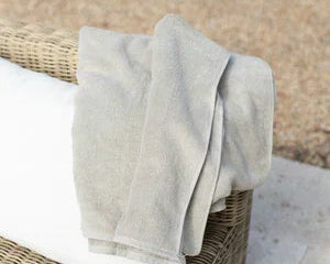 Serviette de piscine beige en tissu doux posée sur un coussin blanc d'un fauteuil en rotin