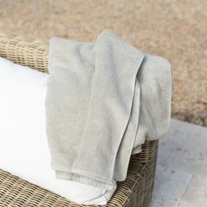 Serviette de piscine beige en tissu doux posée sur un coussin blanc d'un fauteuil en rotin