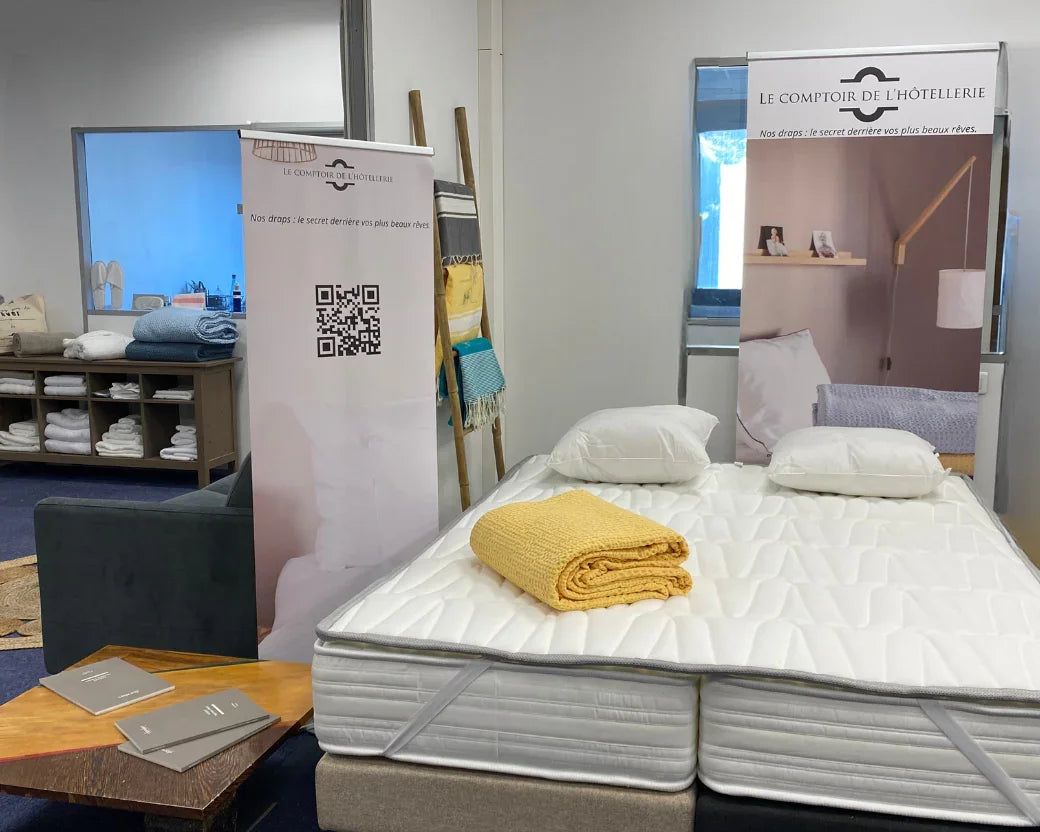 Showroom avec lit double, matelas, oreillers blancs et couverture jaune, décor minimaliste d'hôtel