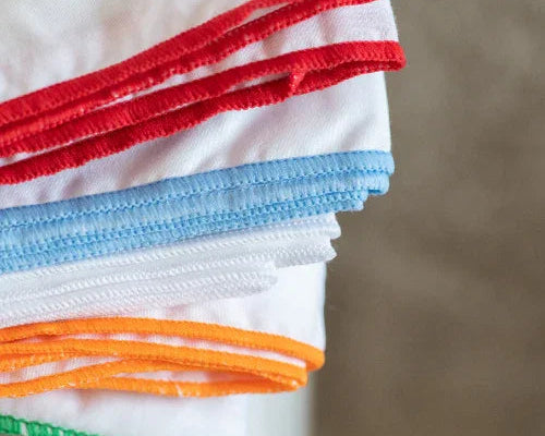 Surjet de coins de tissu blanc avec surpiqûres colorées rouge, bleu, orange et vert sur fond neutre