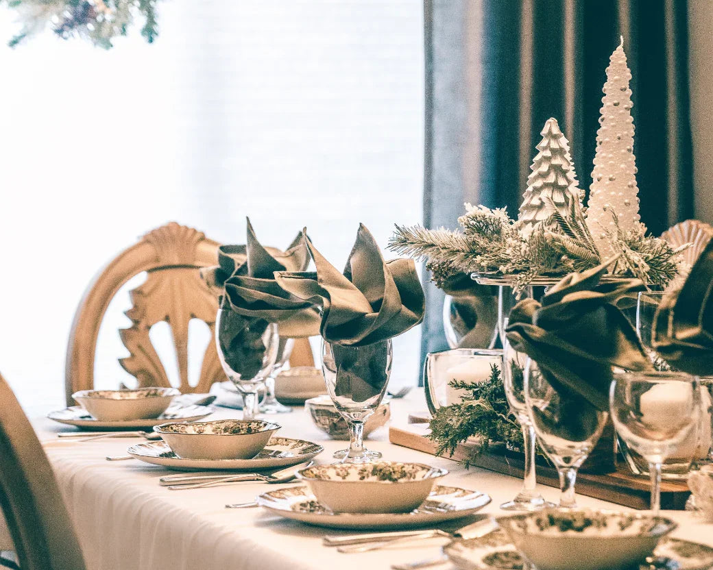 Table de Noël élégante avec vaisselle festive, serviettes pliées, décorations sapins blancs et centre de table vert