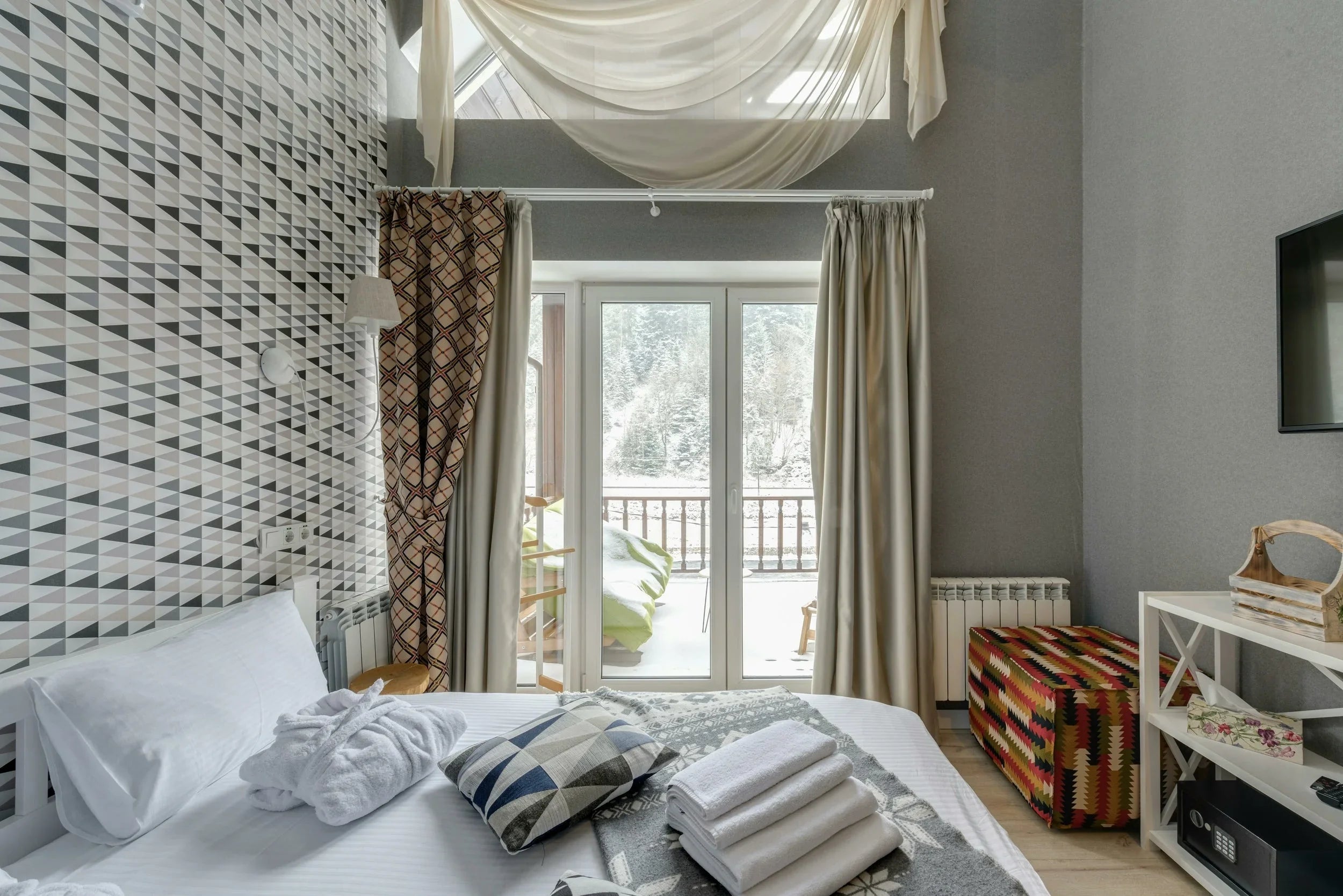 Chambre d'hôtel moderne avec lit blanc, coussin à motifs, balcon et vue sur forêt enneigée