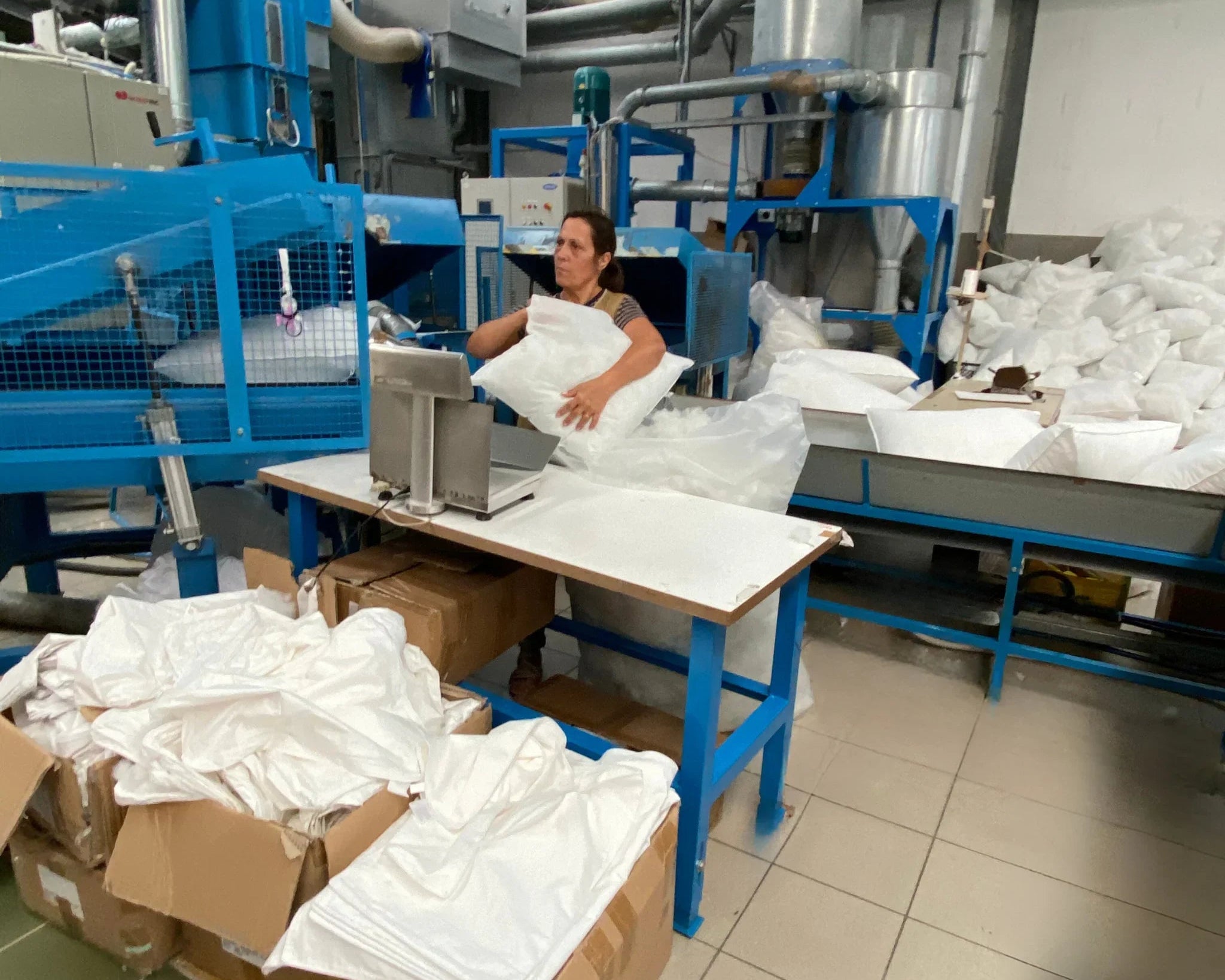 Opératrice dans usine textile emballant oreillers blancs près machine bleue industrielle