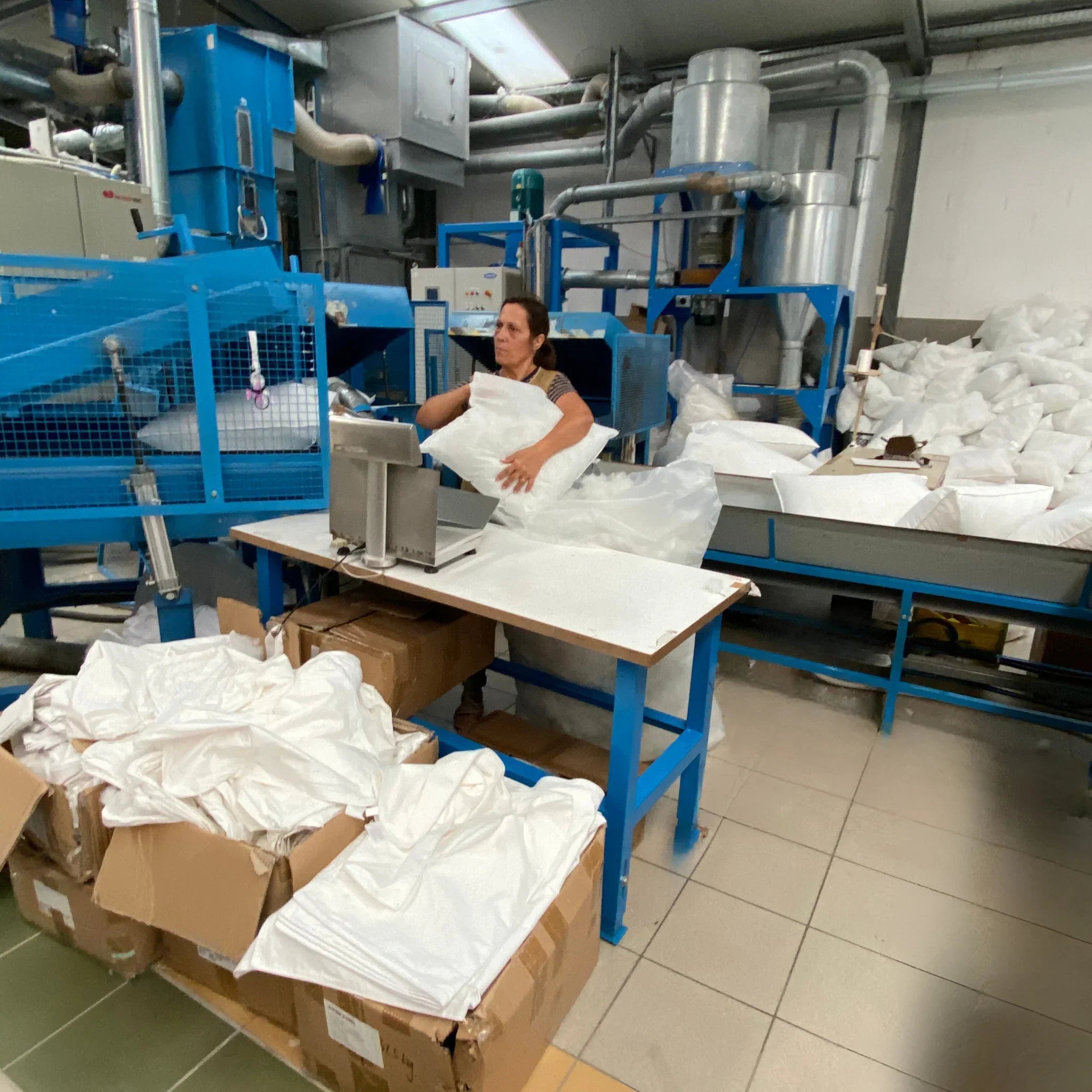 Opératrice dans usine textile emballant oreillers blancs près machine bleue industrielle