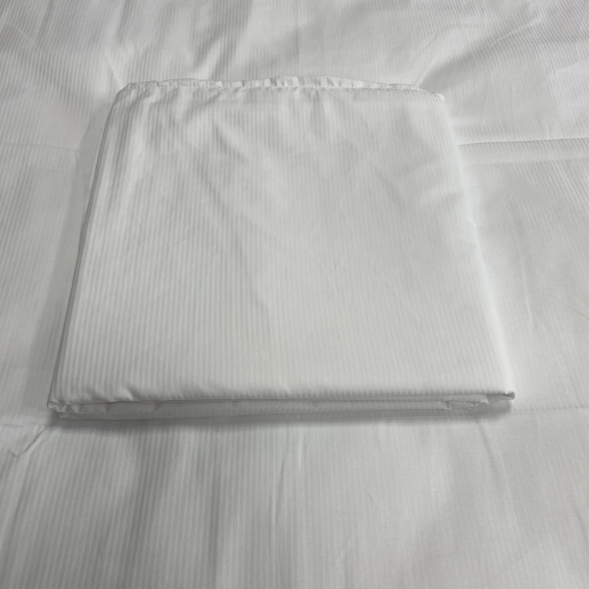 Housse de couette blanche à fines rayures, pliée sur un linge de lit assorti