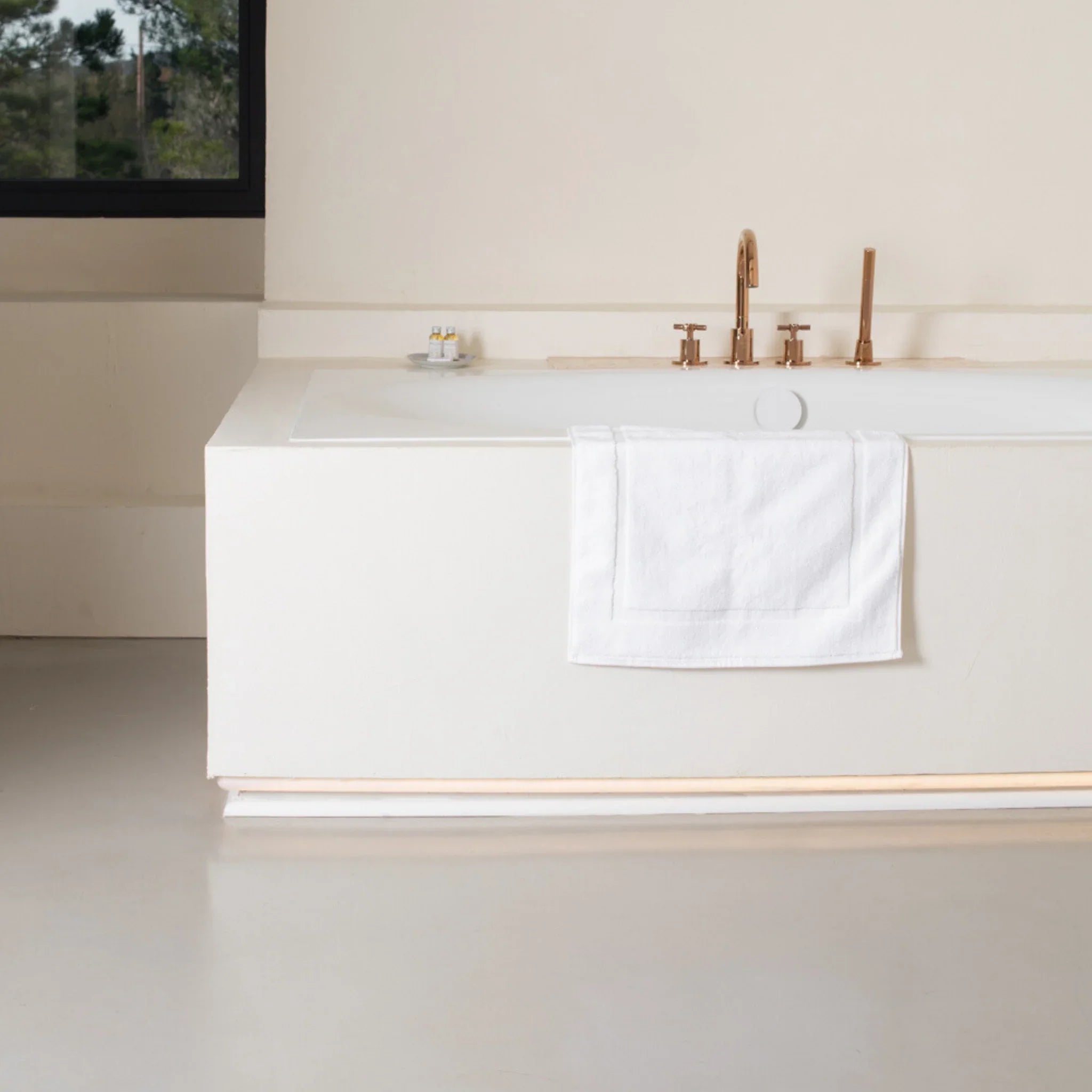 Baignoire blanche moderne avec robinetterie dorée et serviette blanche dans salle de bain minimaliste