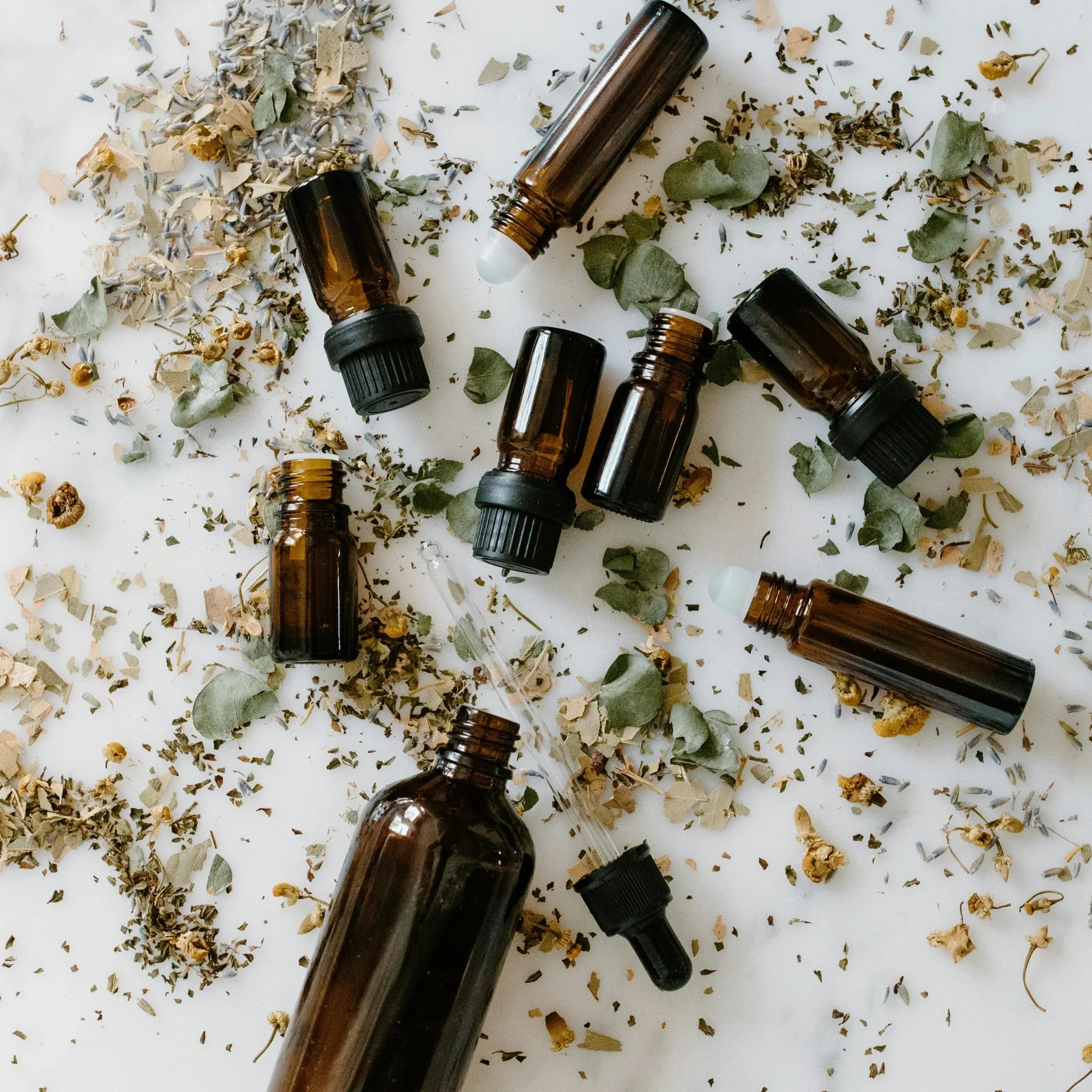 Flacons en verre ambré avec pipette et roll-on entourés de feuilles et fleurs séchées naturelles