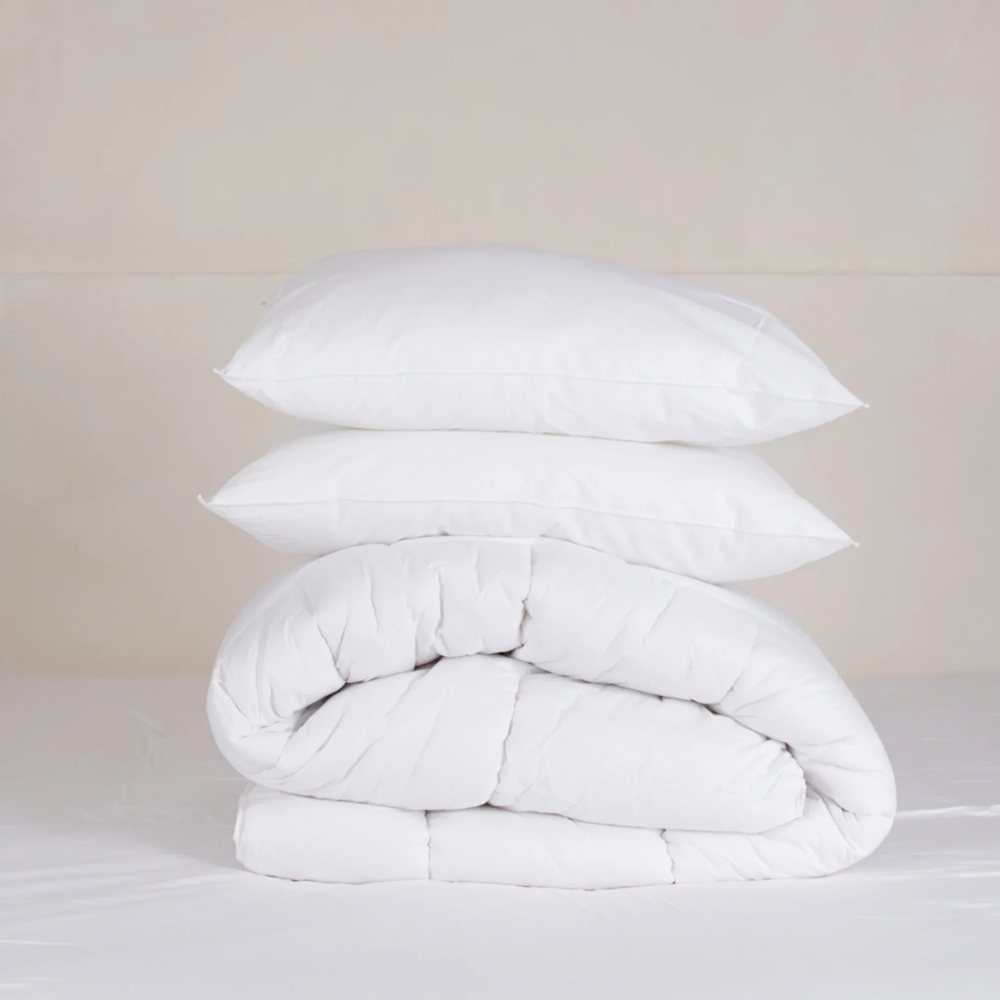 Deux oreillers blancs empilés sur une couette blanche pliée dans un décor minimaliste