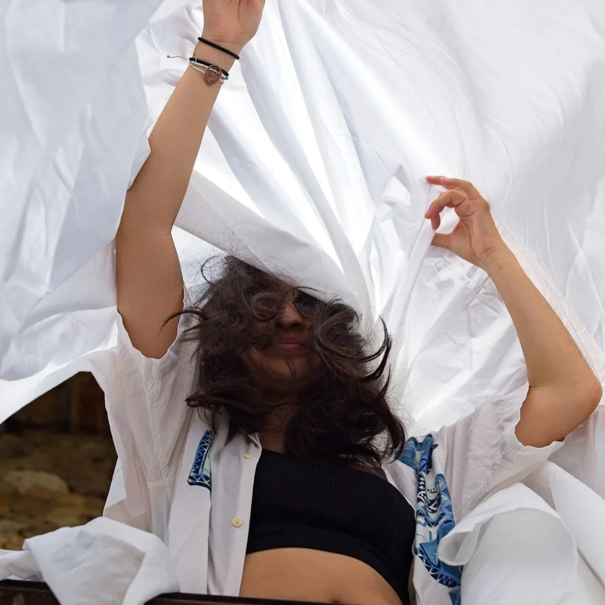 Femme aux cheveux longs et lunettes de soleil déployant un drap blanc en extérieur