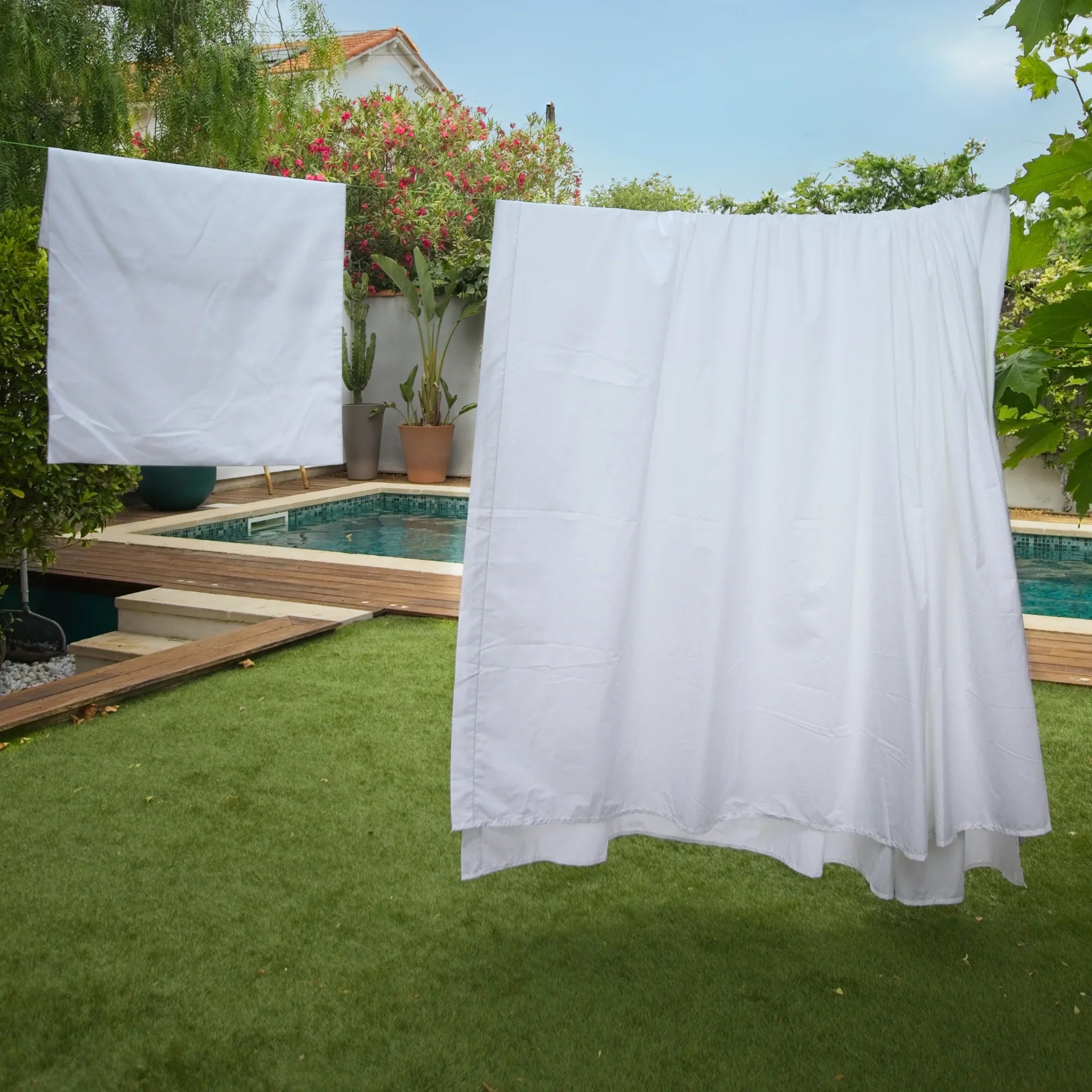 Draps blancs suspendus à sécher dans un jardin avec piscine et végétation