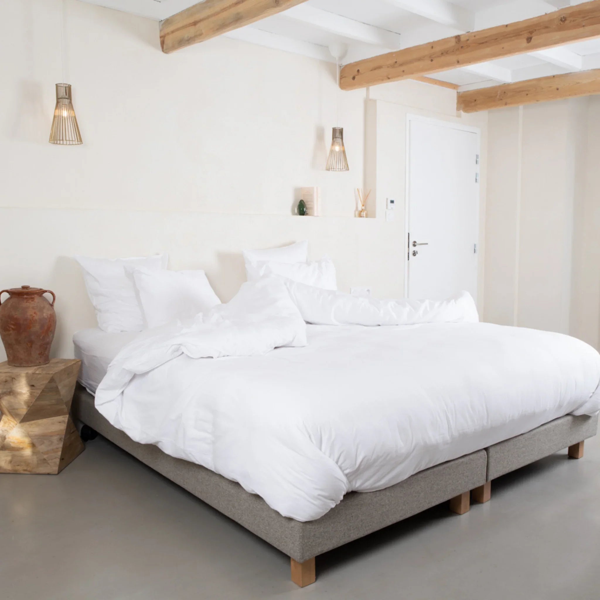 Chambre lumineuse avec grand lit double blanc, cadre gris et déco bois naturel