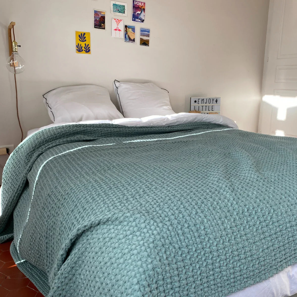 Lit double avec couverture turquoise texturée style nid d'abeille et deux oreillers blancs dans chambre lumineuse minimaliste