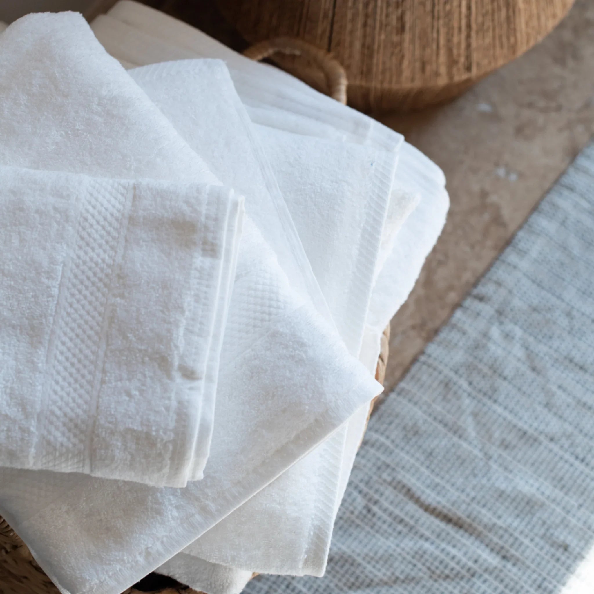 Pile de serviettes blanches en coton dépliées dans un panier tressé sur un sol en pierre