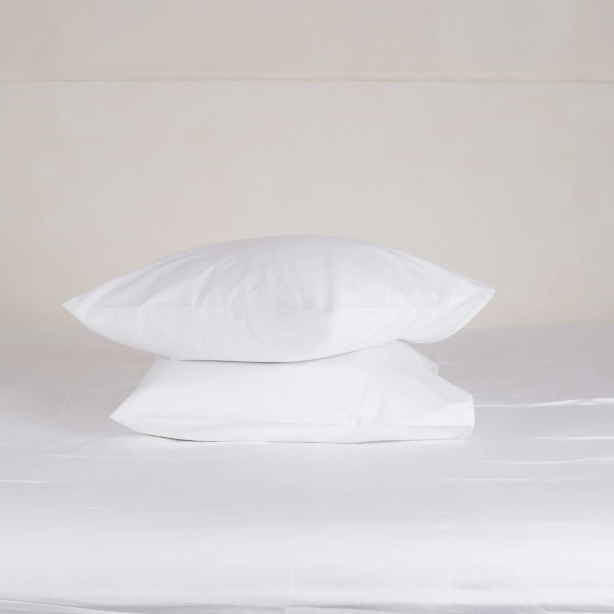 Deux taies d'oreiller blanches superposées sur un lit blanc minimaliste