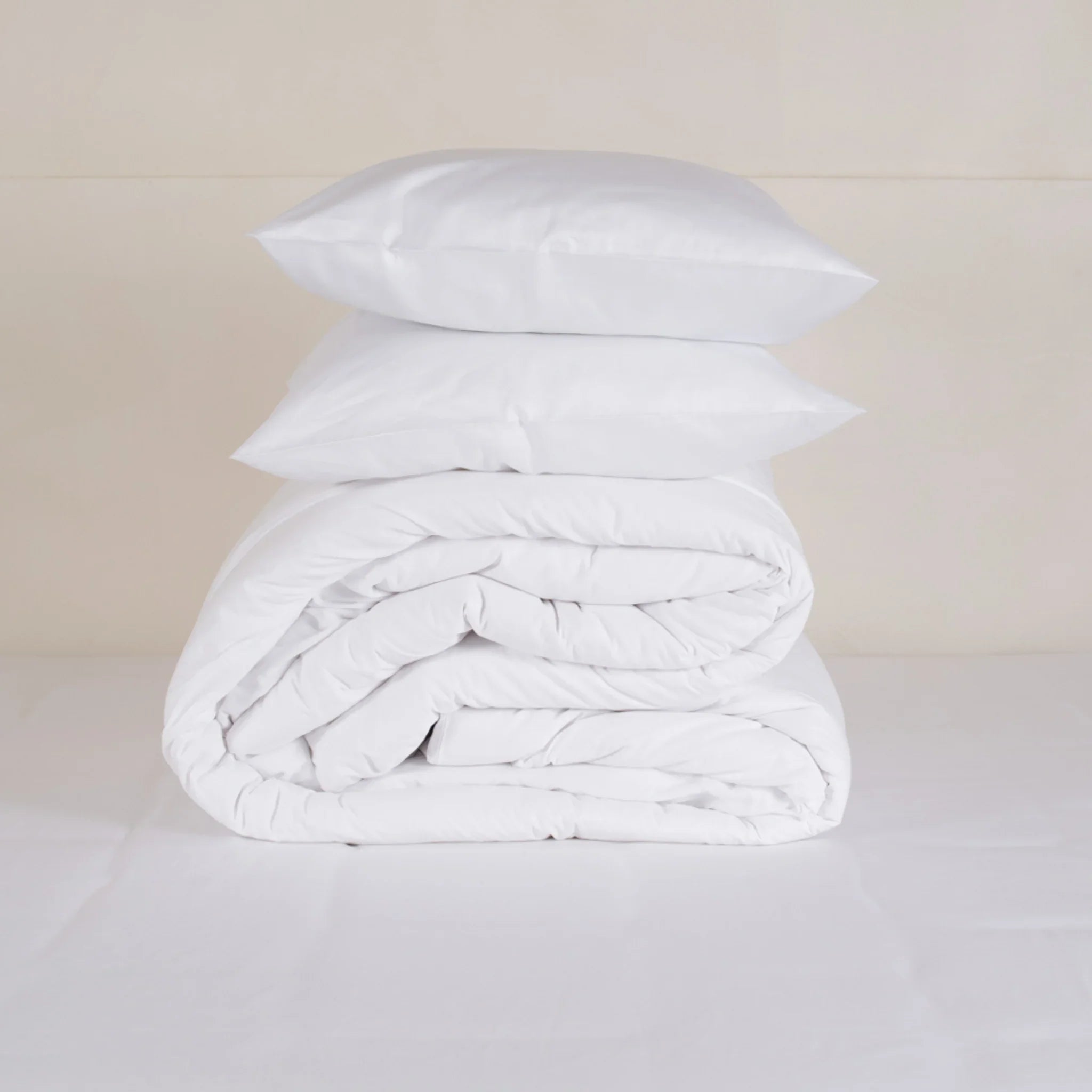 Pile de deux oreillers et d'une couette blanche pliée sur un lit, linge de maison minimaliste